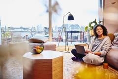 Woman leaning against a couch, sitting on the floor, with laptop on her lap