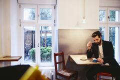 Man sitting at table with a coffee, looking seriously at his phone.