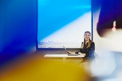 Woman smiling with laptop near window with city view.