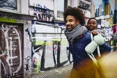 Smiling man with kid on his back walking through a city.
