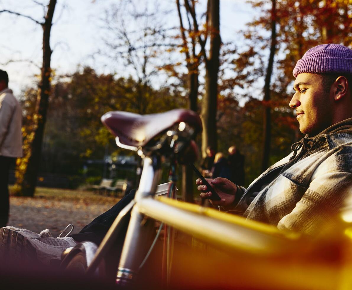 Man sitting on a bench with his bike next to him, looking at his phone.