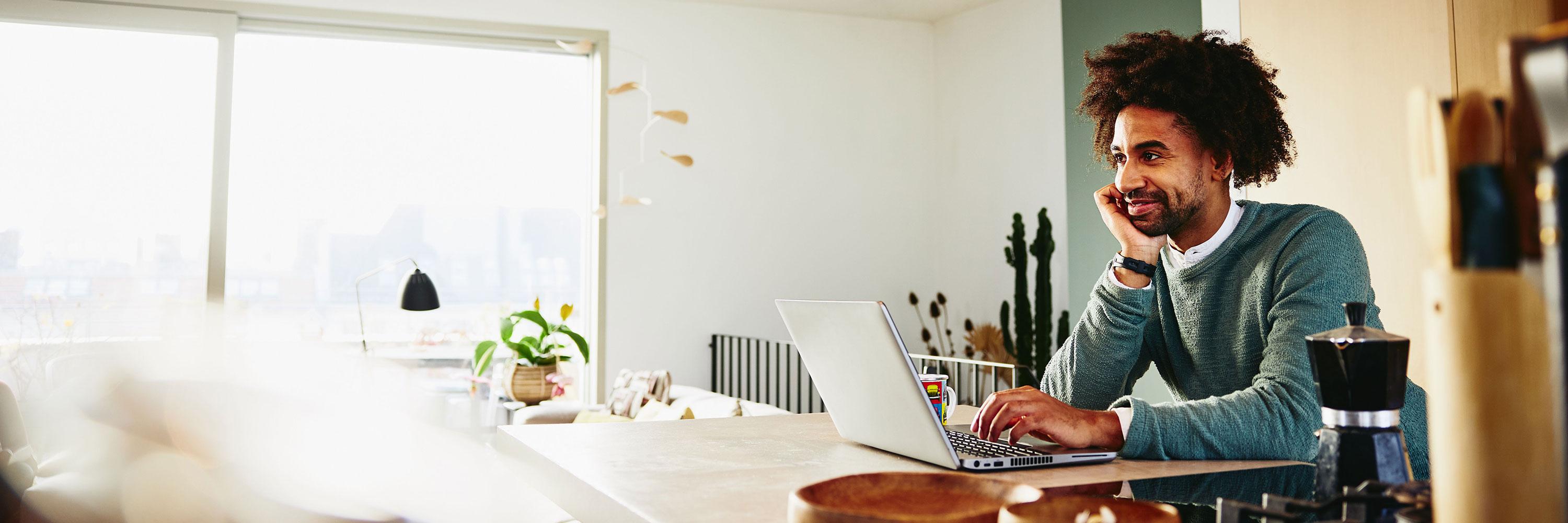 Man leaning against the counter top, while working on laptop.