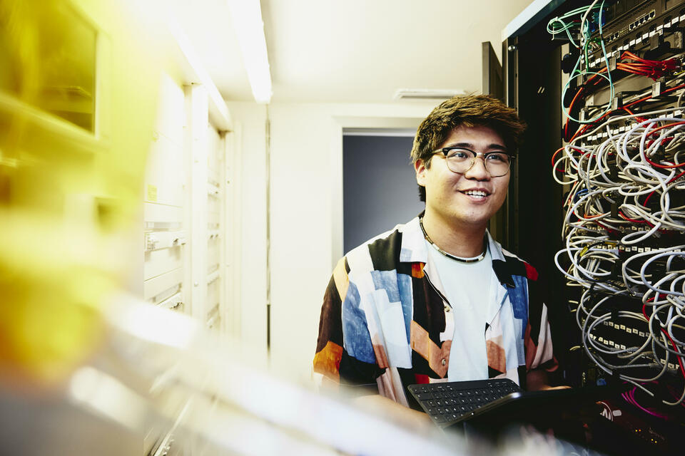 Smiling male holding an tablet standing in a servers room.
